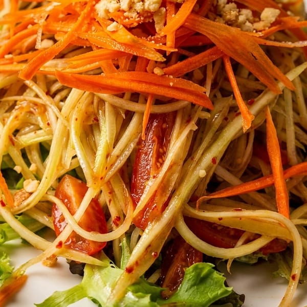Close-up of a vibrant papaya salad with shredded carrots, tomatoes, and peanuts on lettuce.