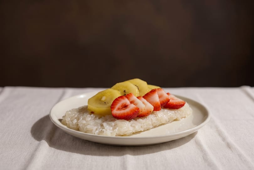 Sticky rice dessert topped with sliced strawberries and golden kiwi on a white plate.
